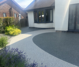 A clean, seamless black and white aggregate resin bound driveway entrance with a contrasting border.